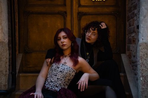 Free Two fashionable women sitting on stone steps in front of an ornate door. Stock Photo