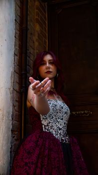 A woman in a gothic lace corset extends her hand in an inviting gesture. Dark and moody.