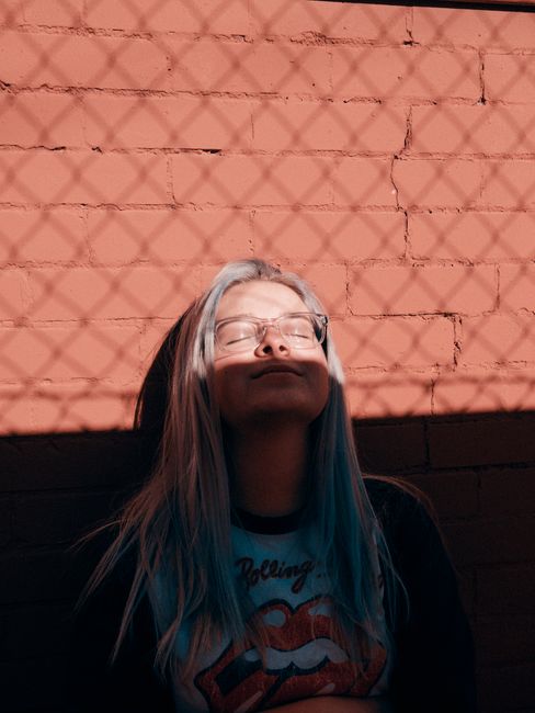 A stylish woman basking in the sun, casting artistic shadows against a brick wall.