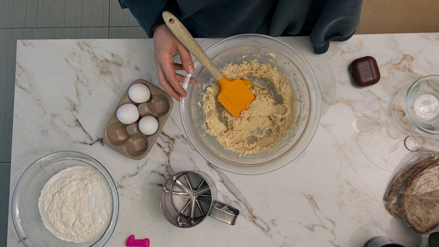 Baking mixture being prepared in a bowl with flour, eggs and kitchen tools