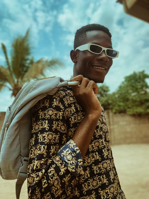 Free Young man wearing sunglasses and patterned shirt, holding backpack outdoors. Stock Photo