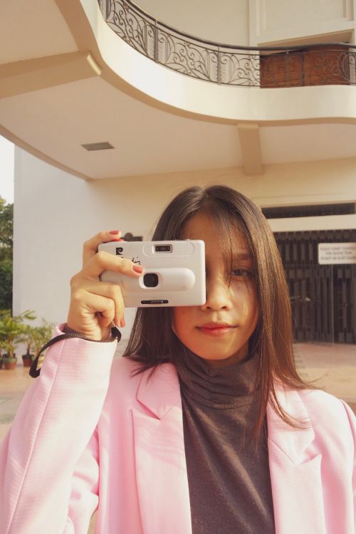 Free Outdoor portrait of a young woman in a pink blazer holding a vintage camera, exuding style and creativity. Stock Photo