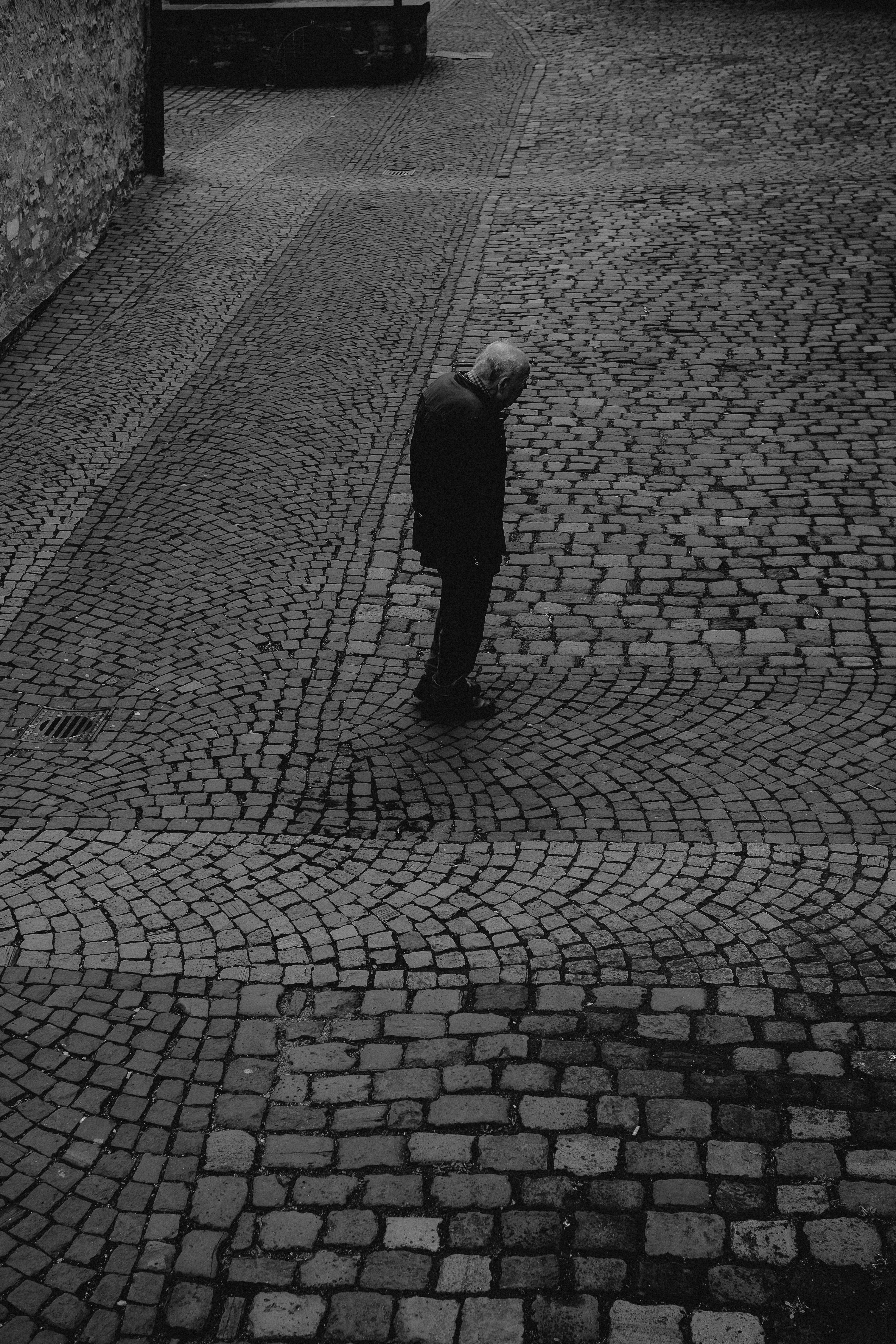 A solitary adult stands on a cobblestone street, captured in a black and white photograph, conveying solitude and introspection.
