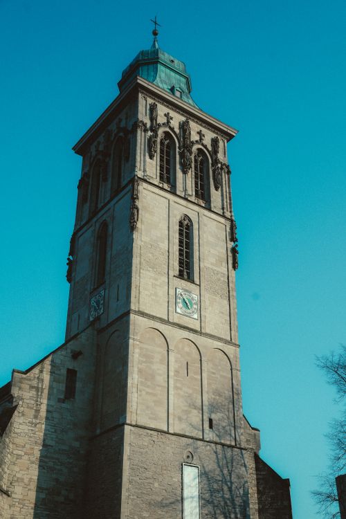 Free Tall, historic stone tower with clock faces under a vibrant blue sky, showcasing architectural detail. Stock Photo