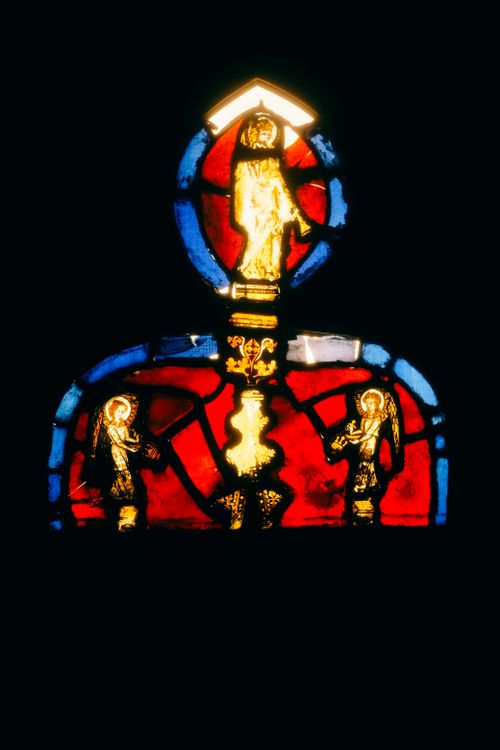 Free Colorful stained glass with religious figures illuminated against a dark backdrop. Stock Photo