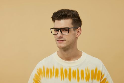 Free Portrait of a confident young man wearing trendy glasses and a tie-dye shirt against a beige backdrop. Stock Photo