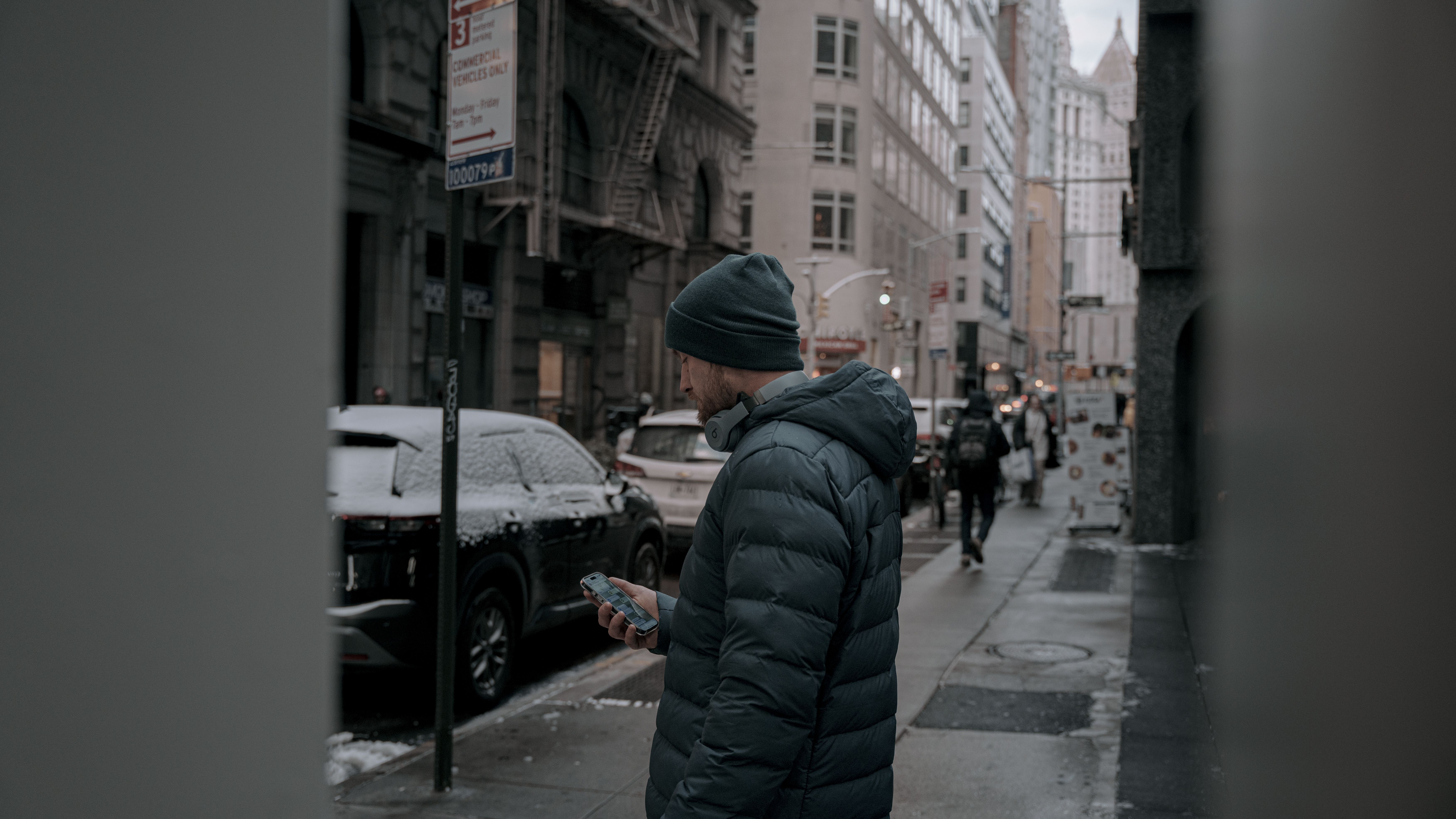 Man in a hooded puffer jacket and knit beanie on a cold New York sidewalk