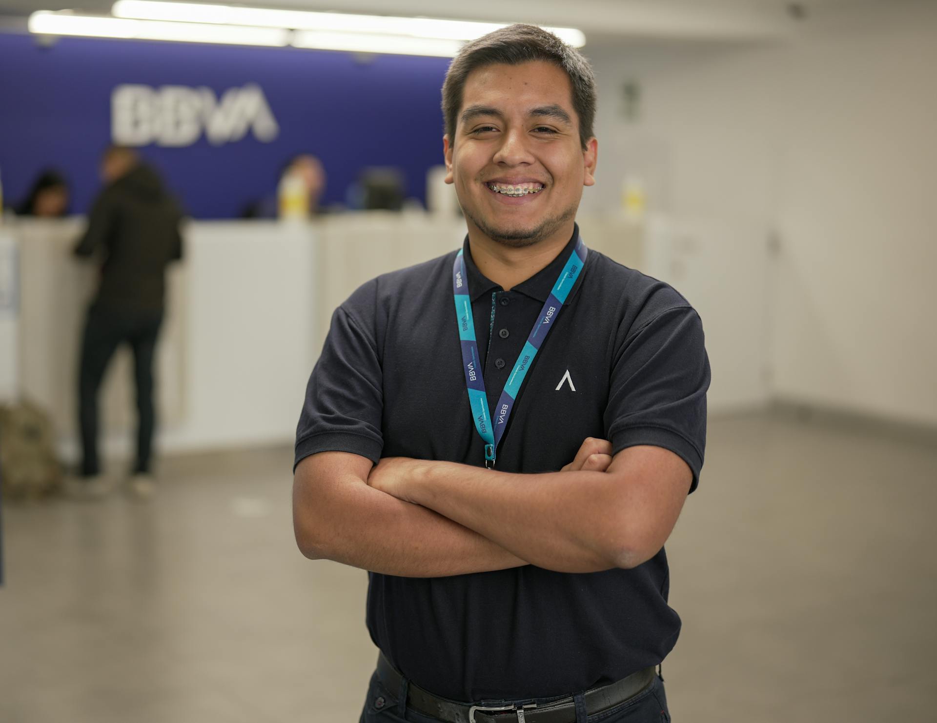 Confident bank employee standing with arms crossed at BBVA reception area, smiling warmly.