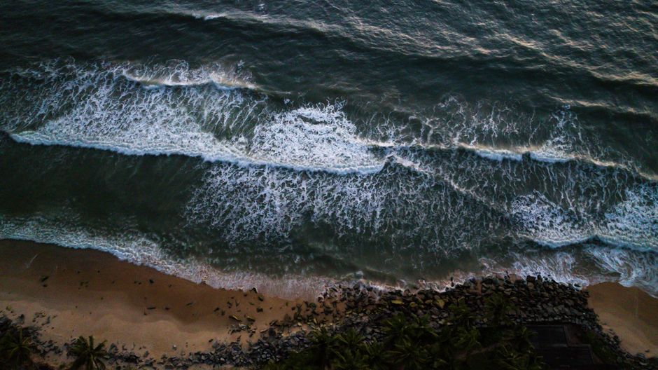 High-angle aerial view of ocean waves hitting a rocky beach at sunset.