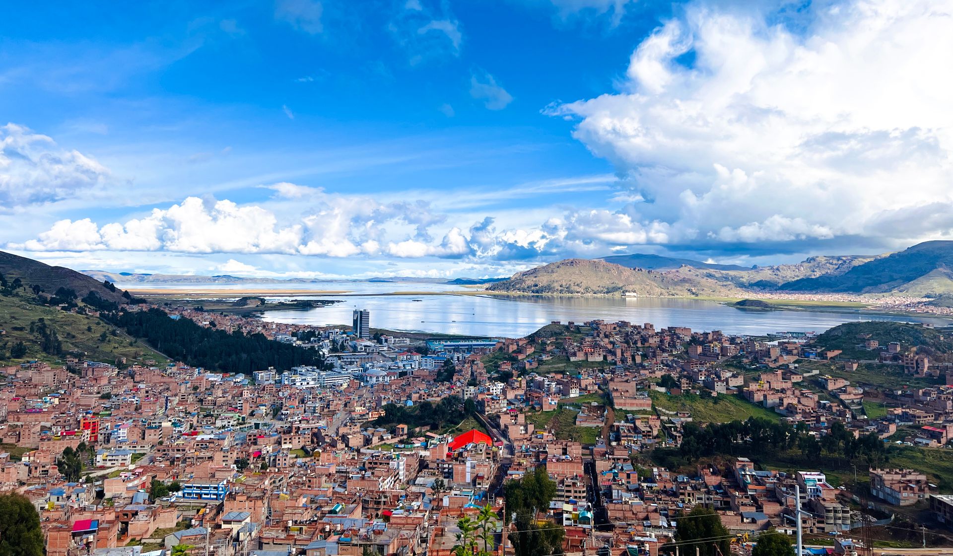 Aerial view showcasing vibrant Puno city against the backdrop of serene Lake Titicaca under a vivid blue sky.