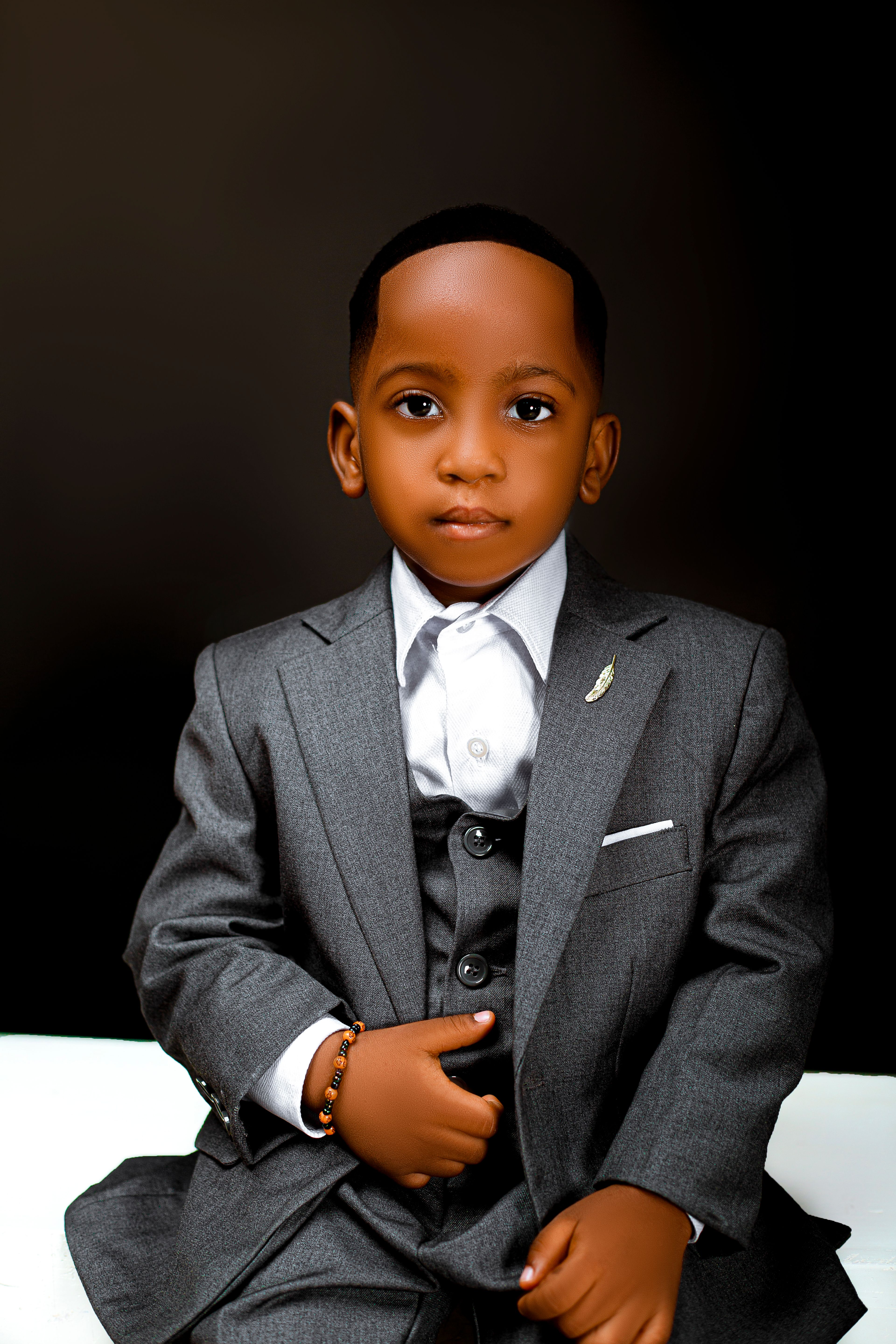 Charming young boy in a tailored suit, exuding confidence and style against a dark background.