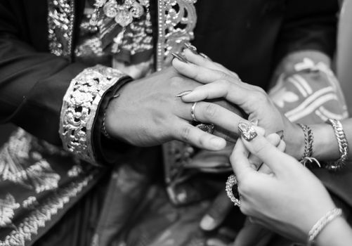 Close-up of a traditional wedding ring exchange in black and white.