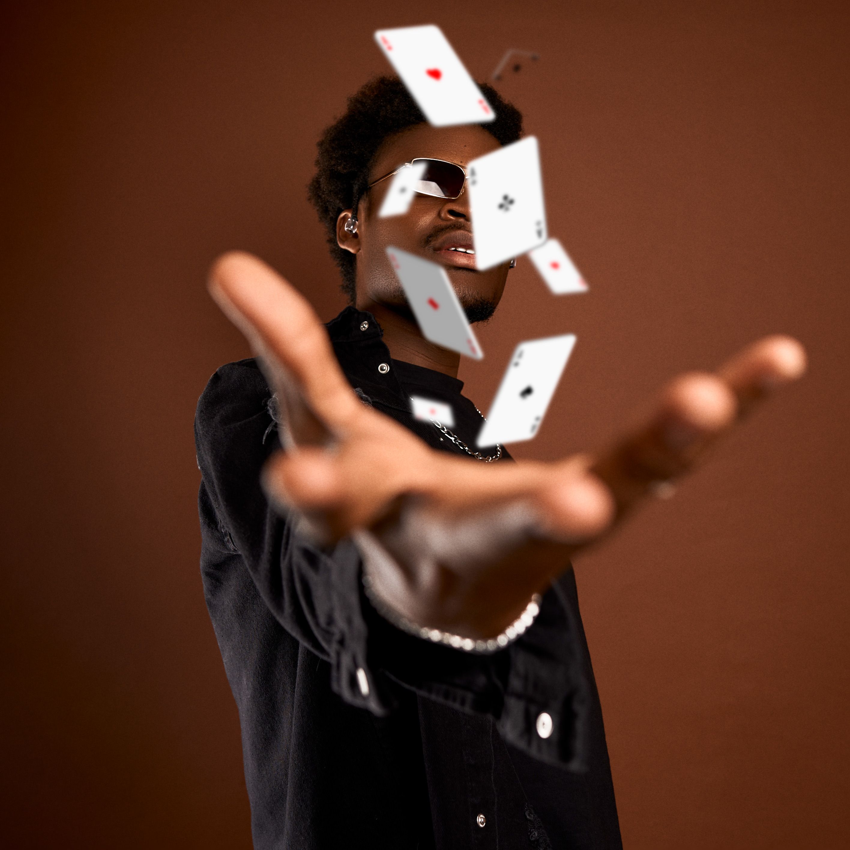 Fashionable man throws playing cards dramatically in a studio setting, capturing movement and style.
