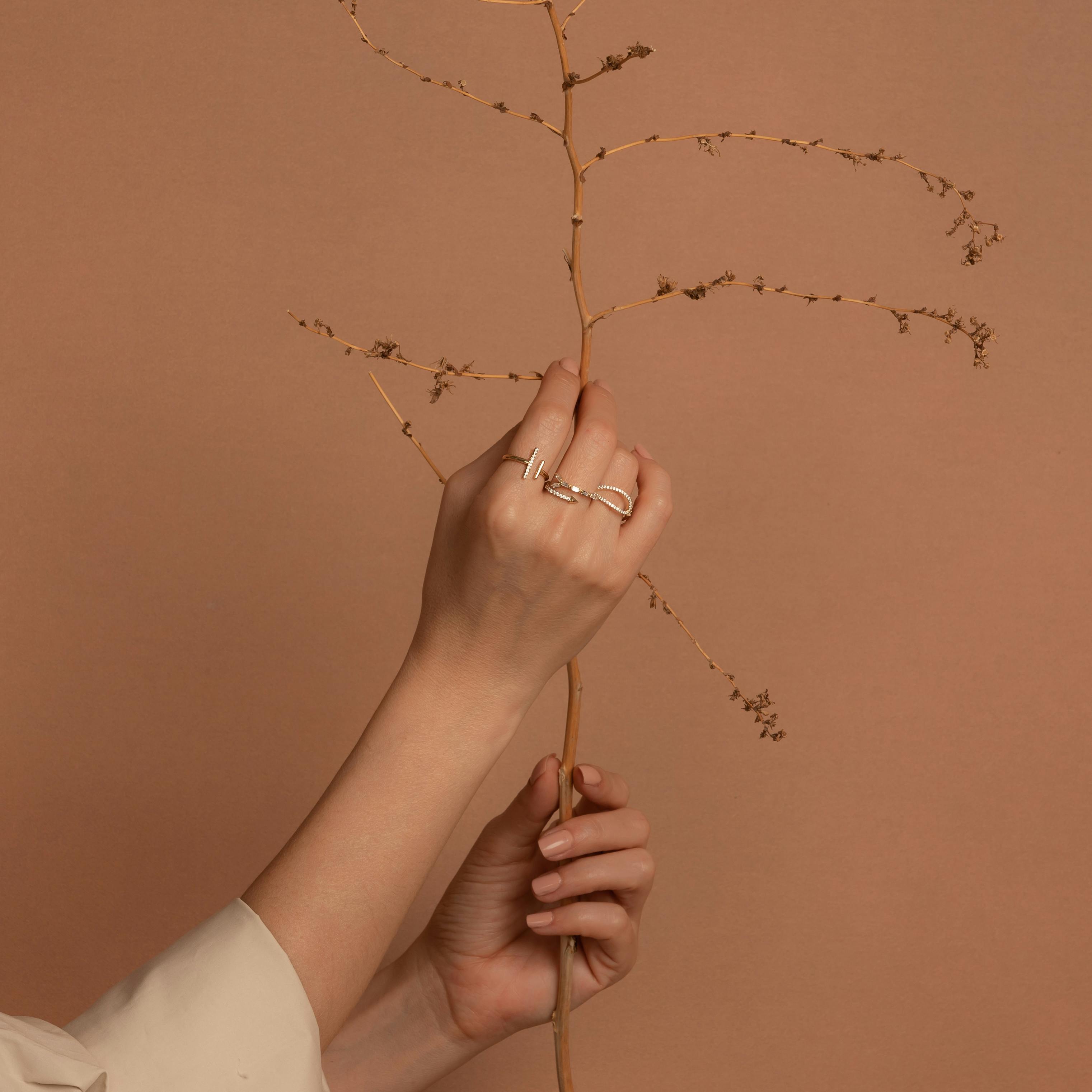 Elegant minimalist jewelry showcased on hand holding a delicate dried branch.