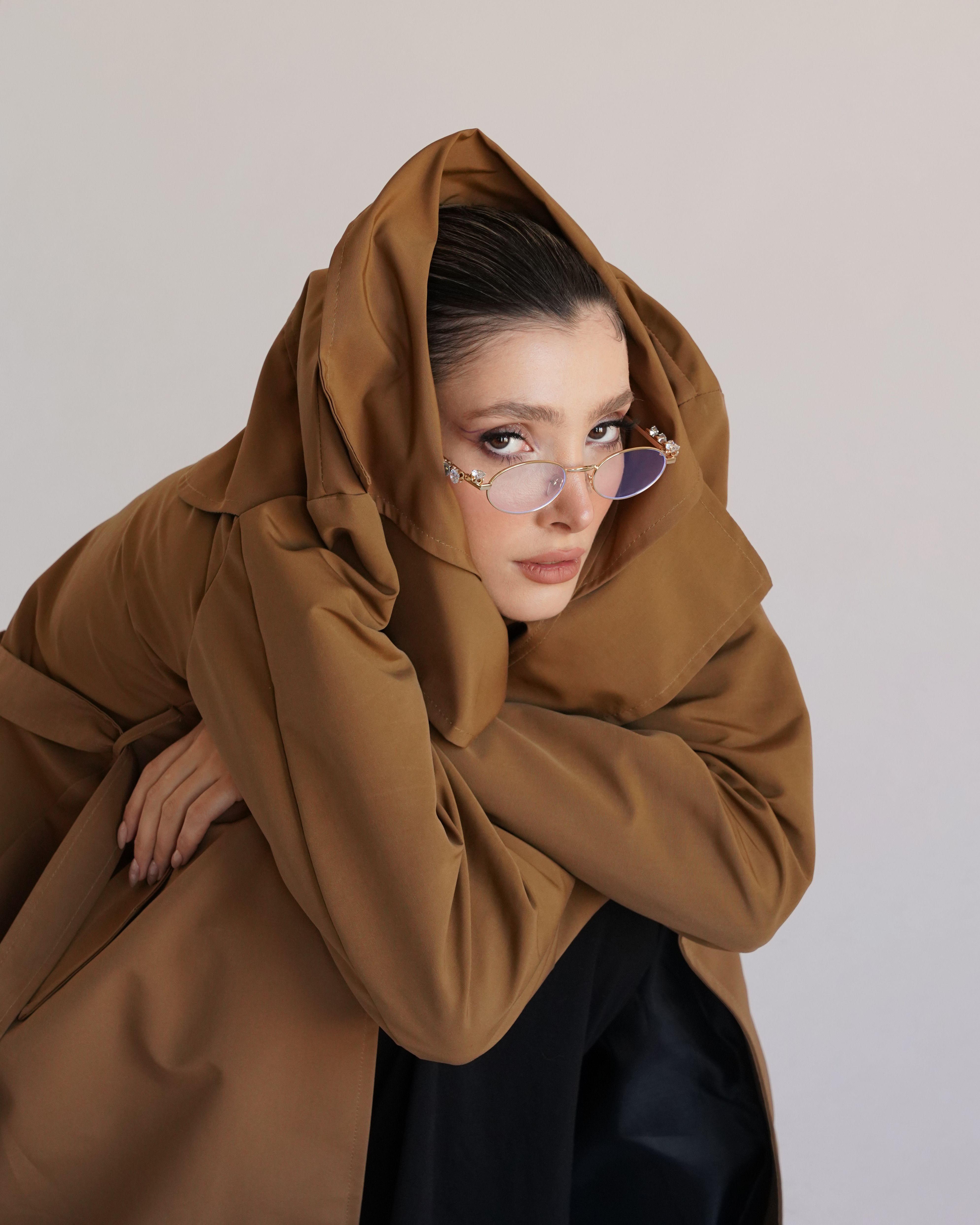 Fashionable woman in a brown coat with sunglasses poses indoors.