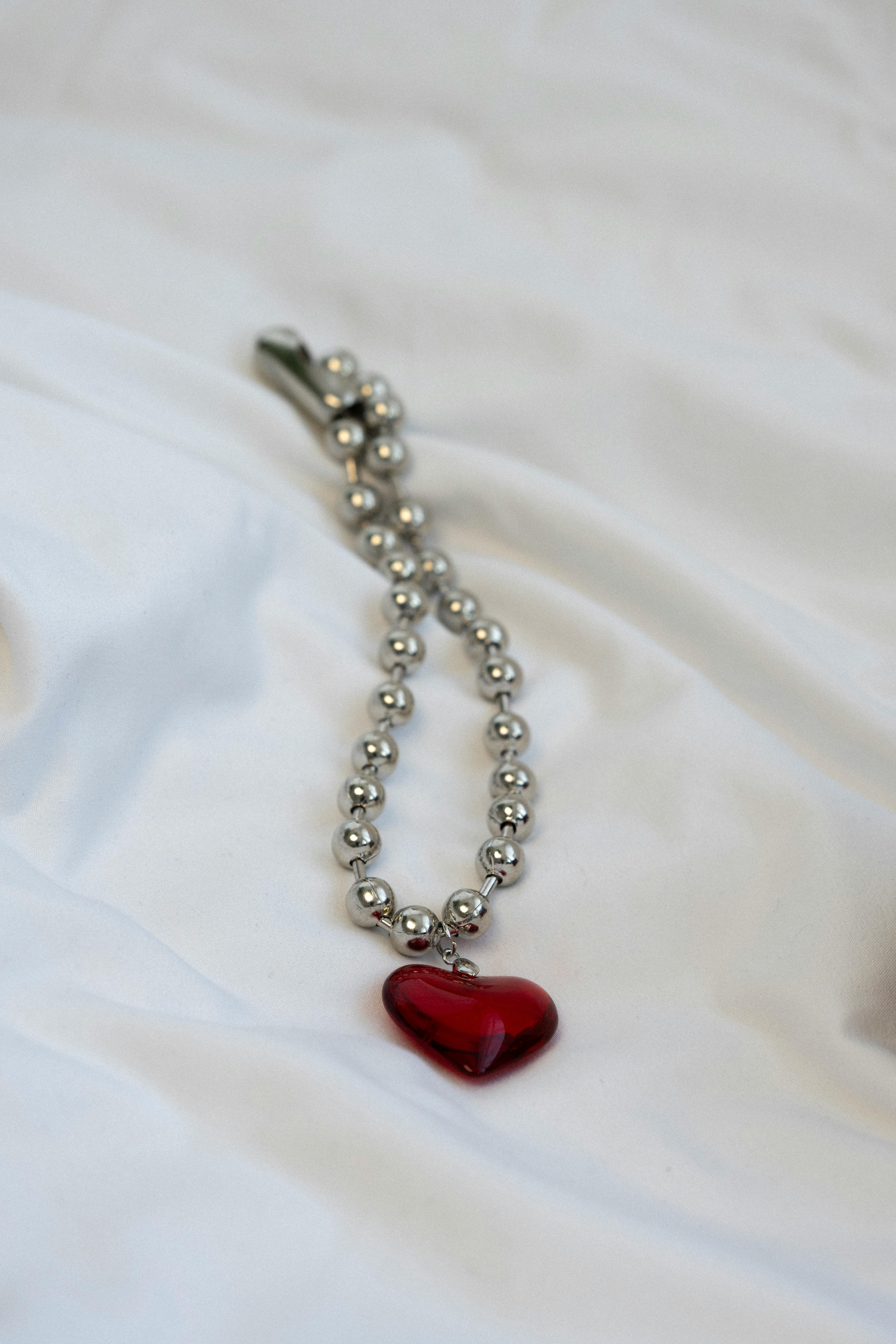 Close-up of a heart-shaped pendant on a silver beaded chain against a soft white background.