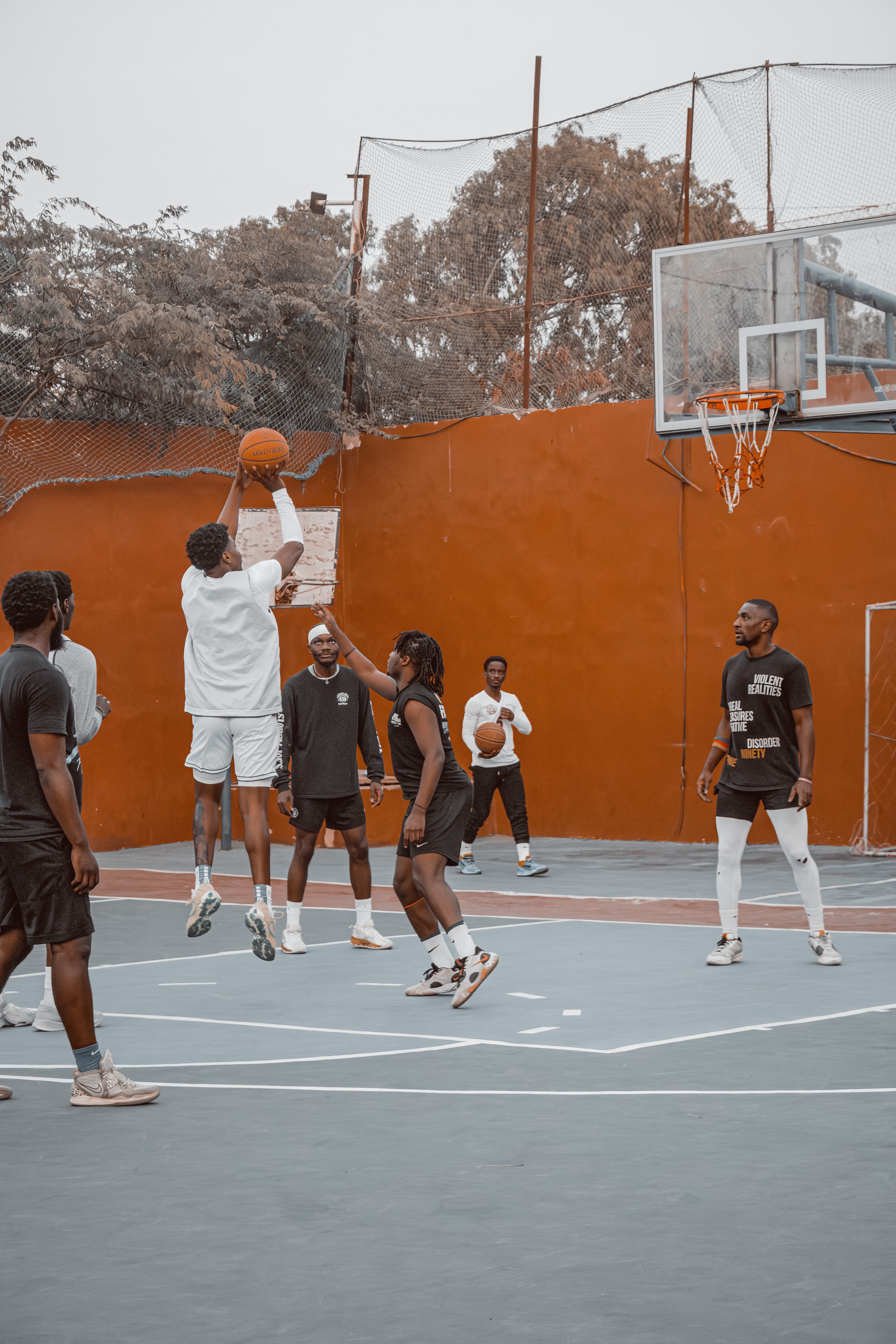 Diverse group of adults playing basketball outdoors on a court, capturing action and teamwork.