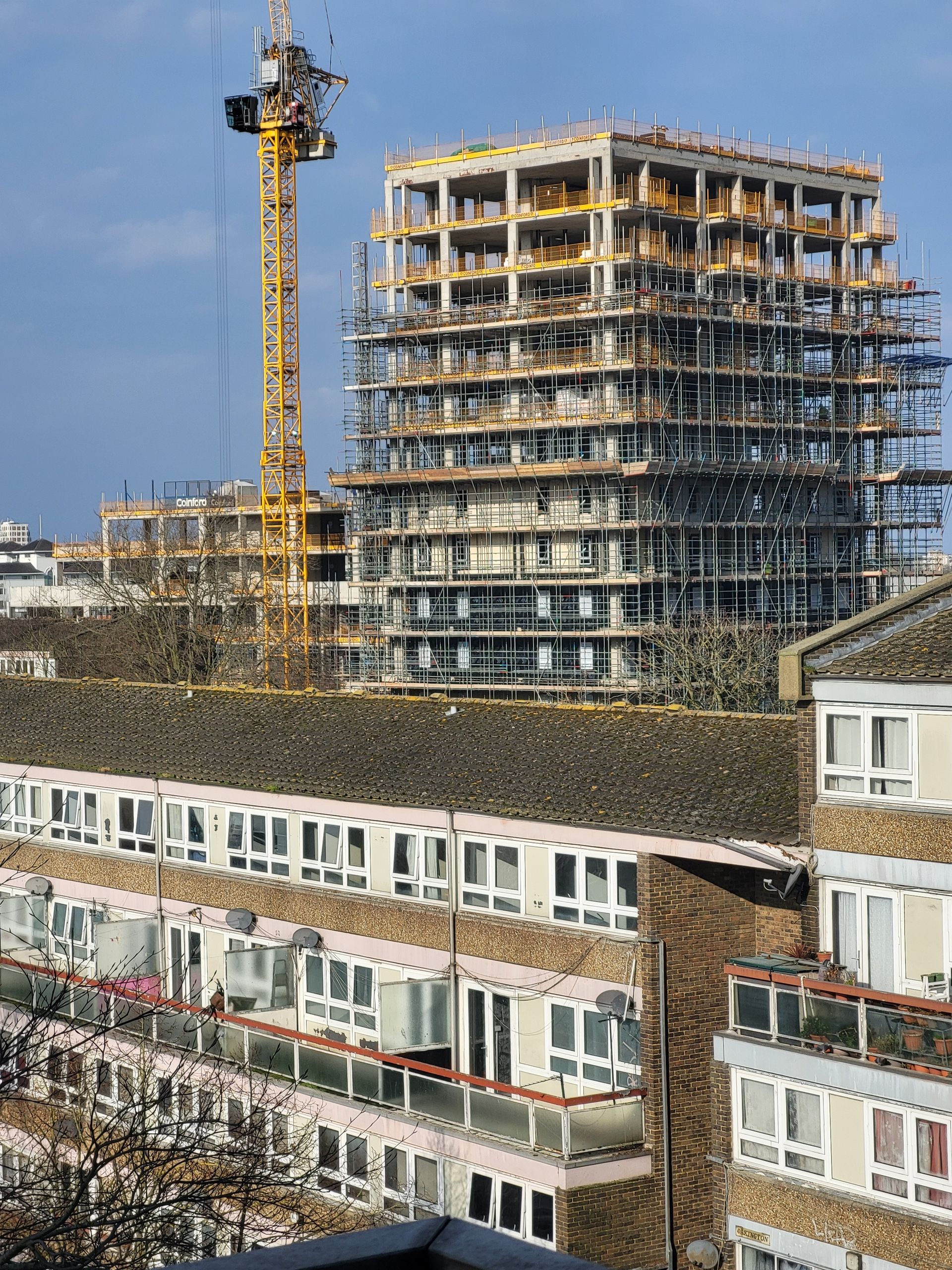 High-rise building under construction with yellow tower crane and scaffolding against urban sky (daytime, wide)