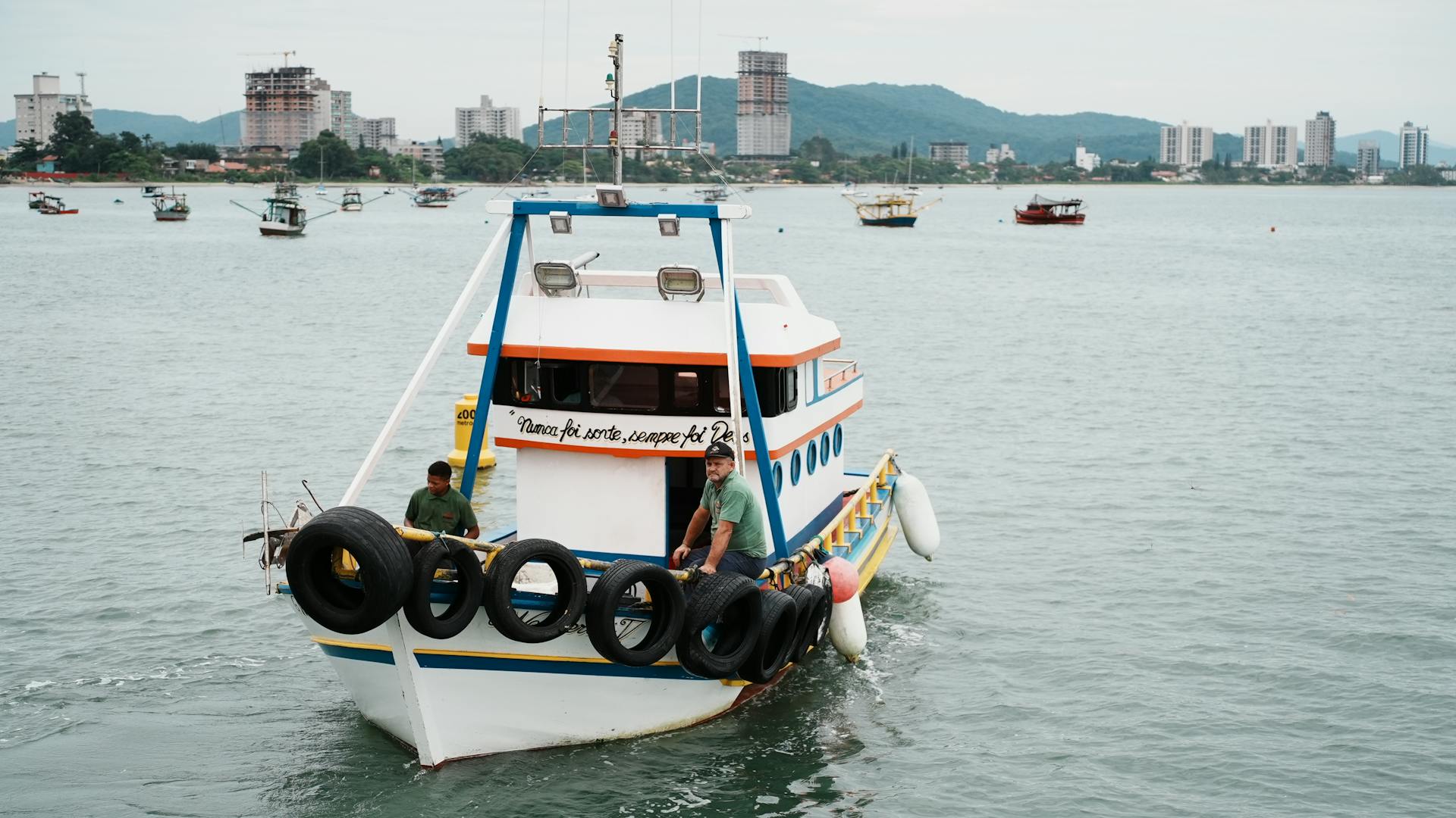 A vibrant fishing boat returns to dock with scenic city skyline in the background, capturing coastal life.