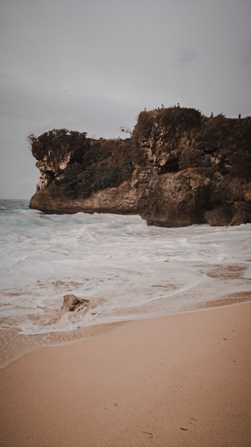 Free Peaceful coastline with rocky cliffs and gentle waves on a sandy beach under an overcast sky. Stock Photo
