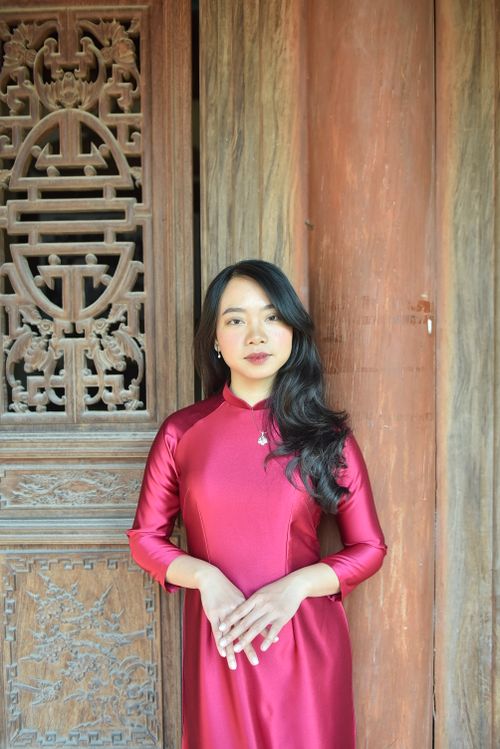 Free Woman in traditional red dress standing by an intricately carved wooden door. Stock Photo