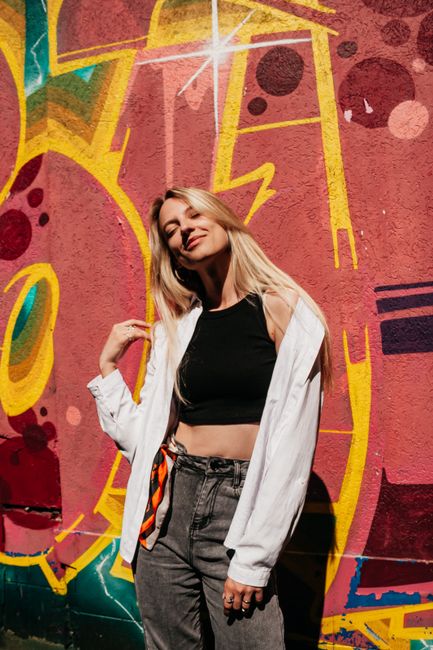 Confident young woman stands stylishly against a vibrant graffiti wall in daylight.