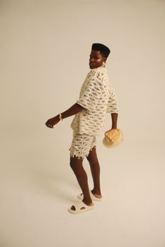 Stylish adult wearing crochet outfit and holding a wicker bag against a simple backdrop.