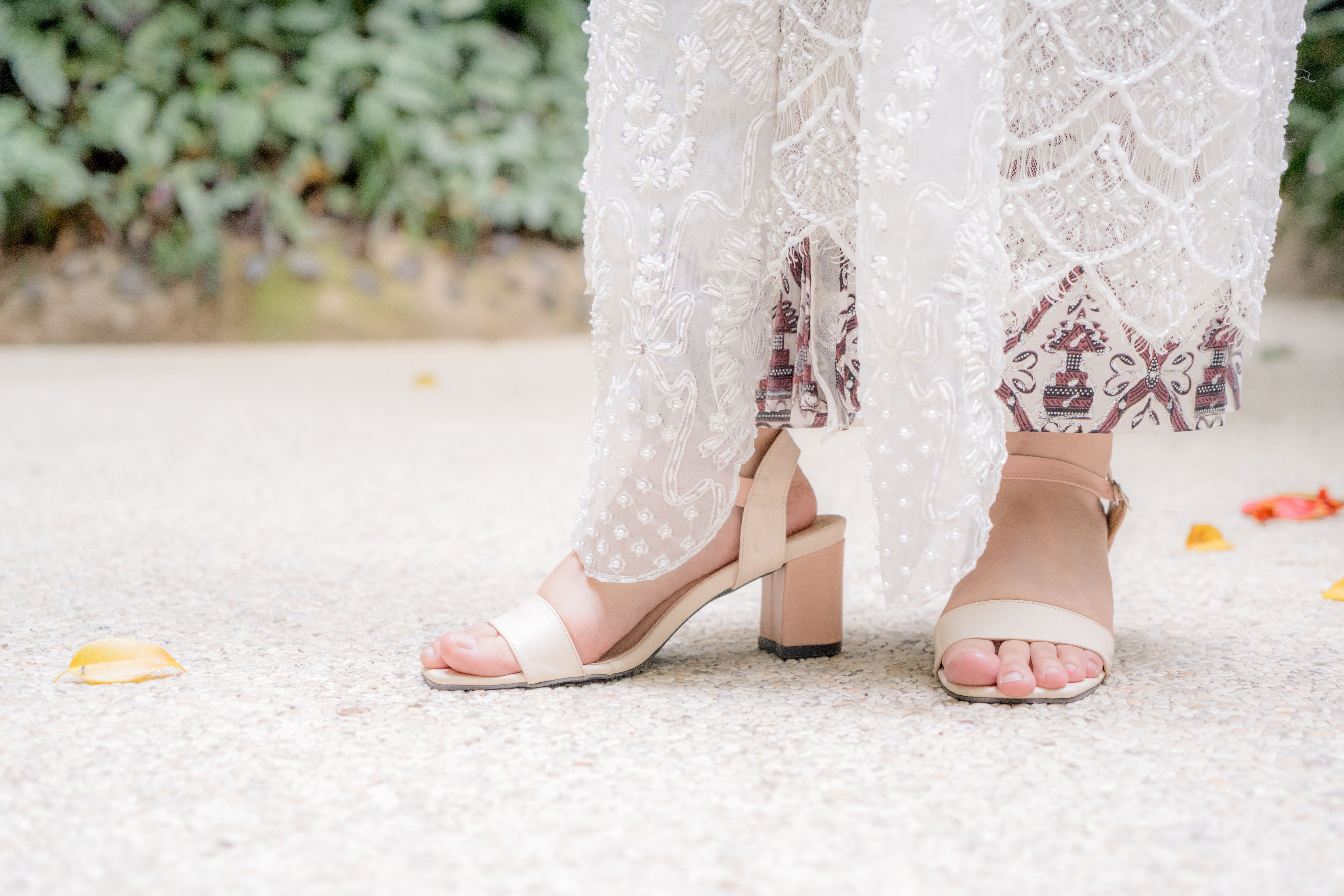 Elegant bridal shoes and delicately embroidered dress in outdoor setting, capturing classic fashion.