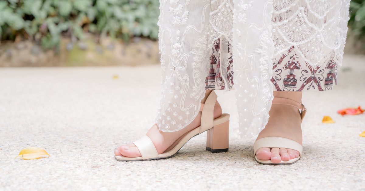 Elegant bridal shoes and delicately embroidered dress in outdoor setting, capturing classic fashion.