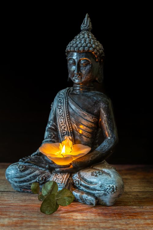 Free Buddha statue holding a glowing candle, symbolizing peace and meditation. Stock Photo