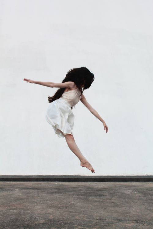 Free A woman in a white dress captured mid-jump against a minimalist white backdrop, embodying freedom and movement. Stock Photo