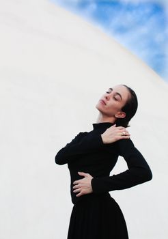 A woman in a black outfit poses gracefully outdoors with a serene expression.