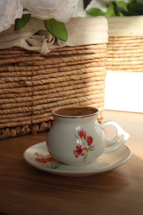 Free Floral ceramic coffee cup filled with coffee on a wooden table with wicker decor. Stock Photo
