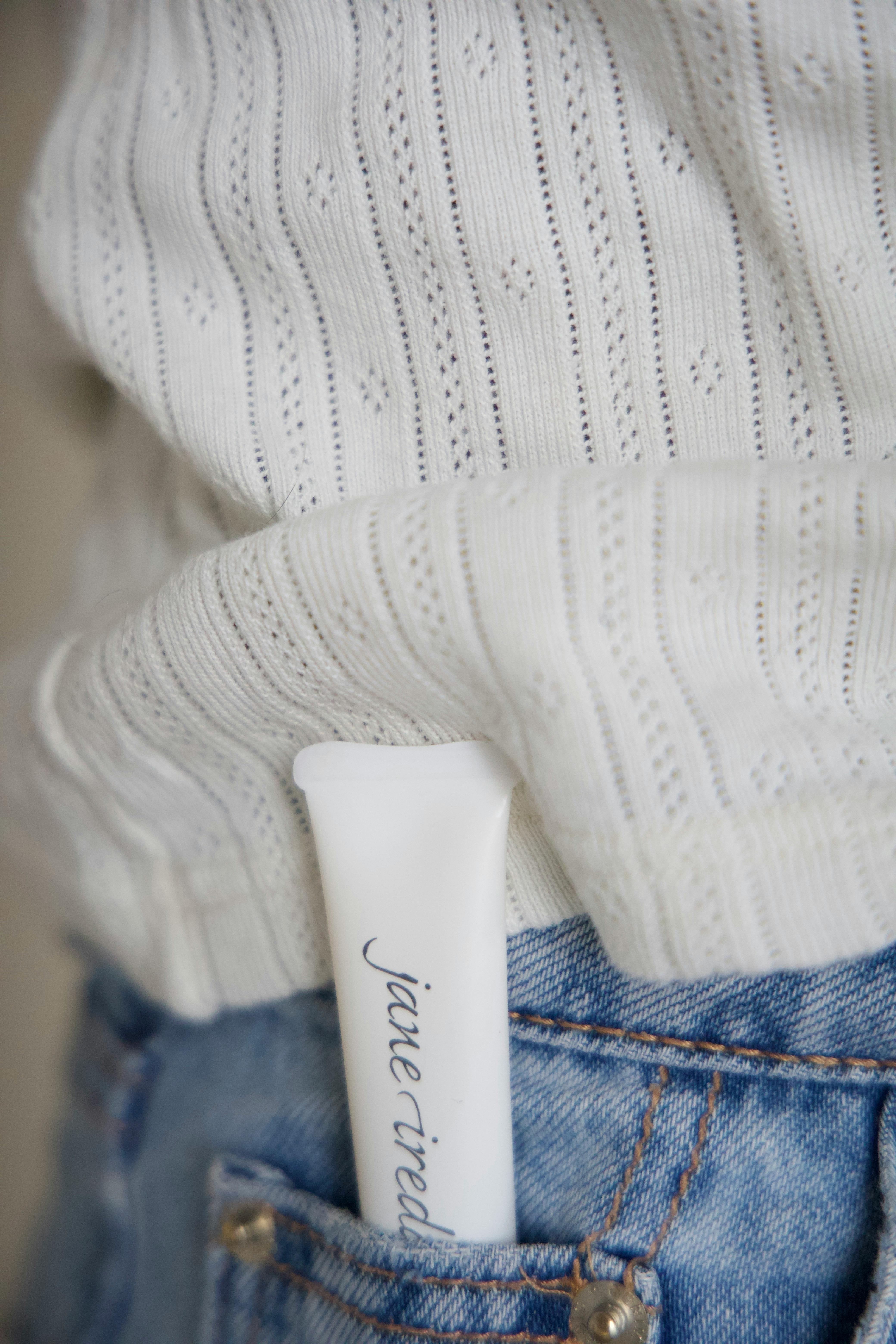 Close-up of a cosmetic tube in a denim pocket, featuring minimalist fashion details.