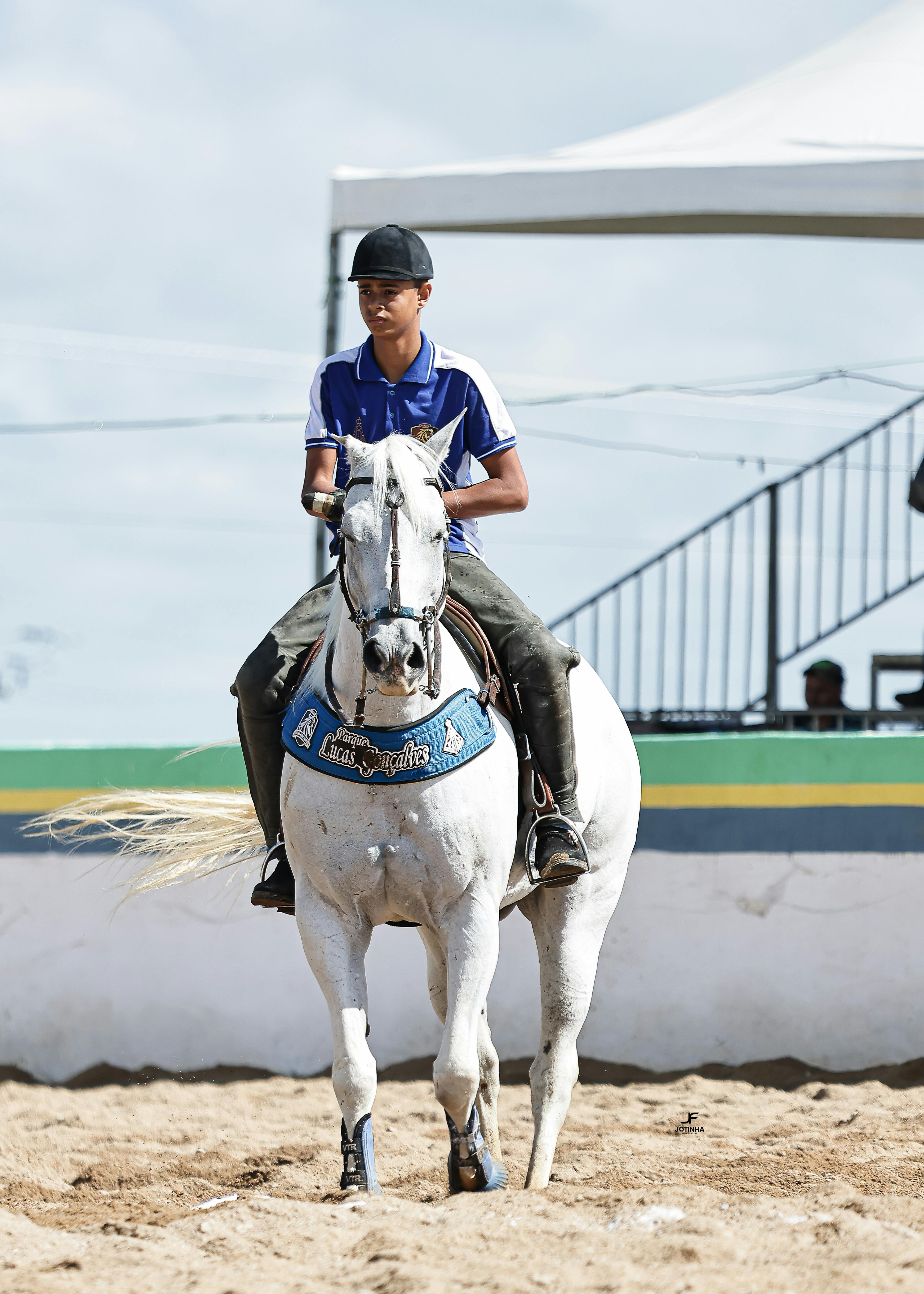 Young male equestrian riding a white horse in a sandy arena during a competition.