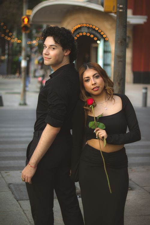 Free Fashionable couple poses in an urban street, holding a red rose, conveying romantic vibes. Stock Photo