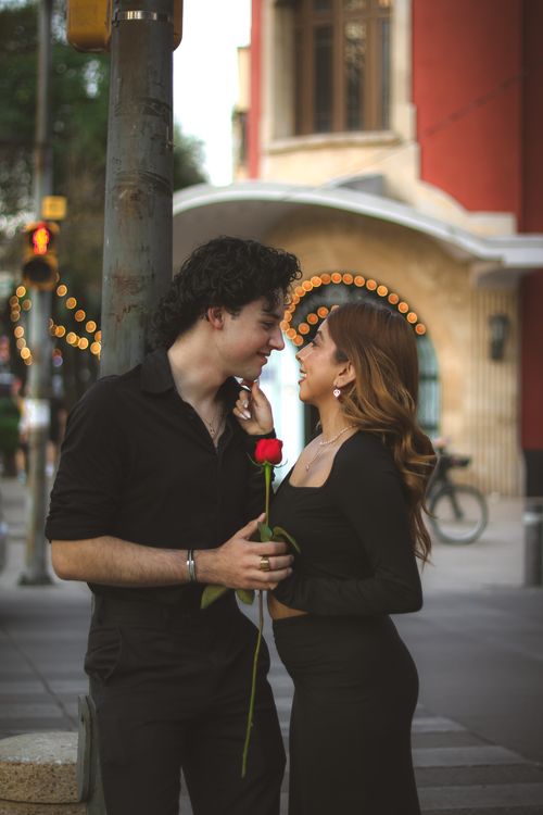 Free A loving couple gazes into each other's eyes with a red rose on a bustling city street. Stock Photo