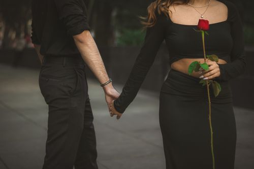 Free A couple in black attire holds hands, symbolizing love and connection with a red rose. Stock Photo