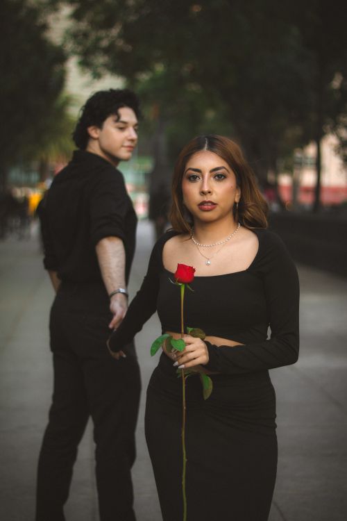 Free A couple in black attire holds a rose, creating a romantic mood on an urban street. Stock Photo