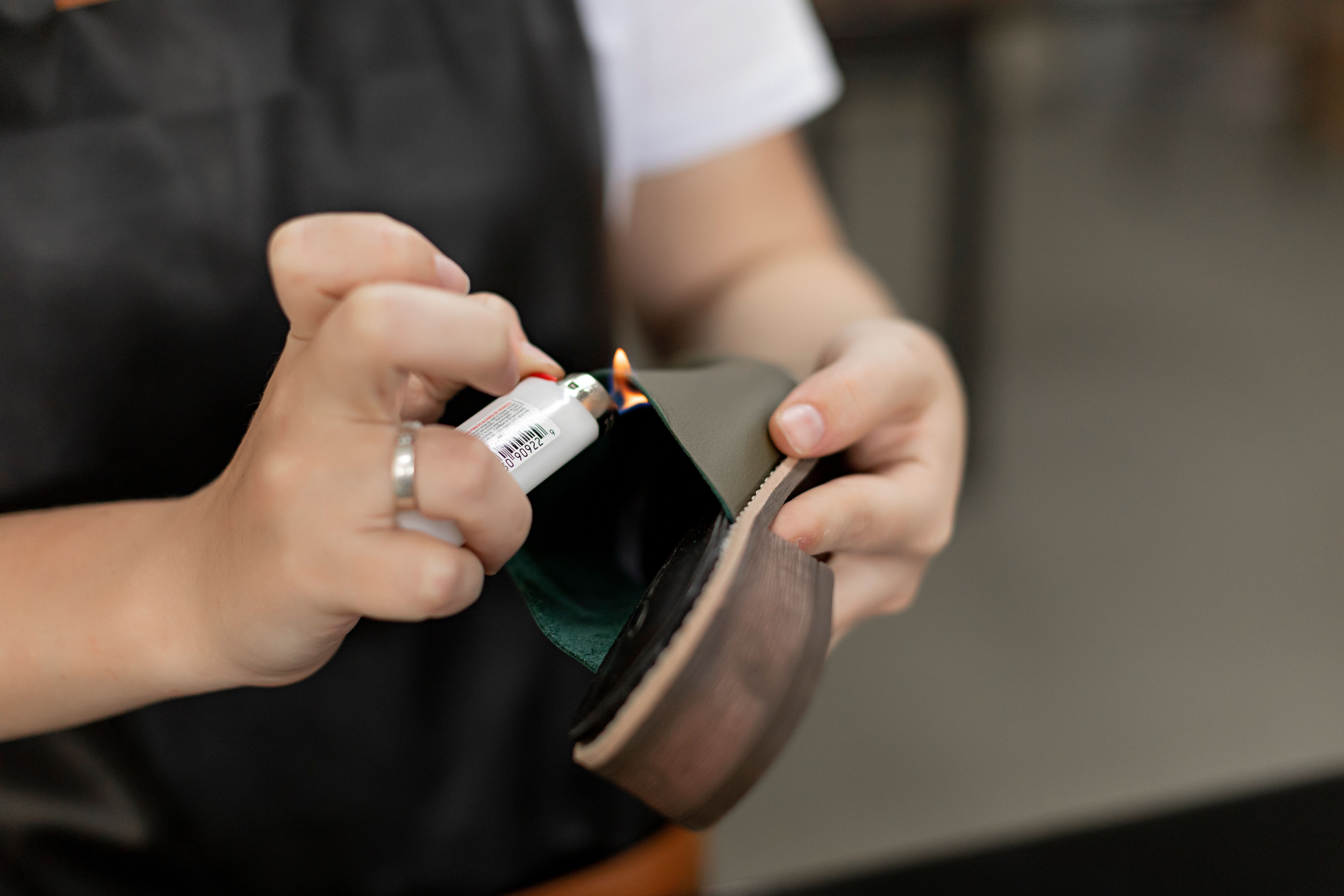 Detail of hands using a lighter for handmade shoe repair in a workshop.