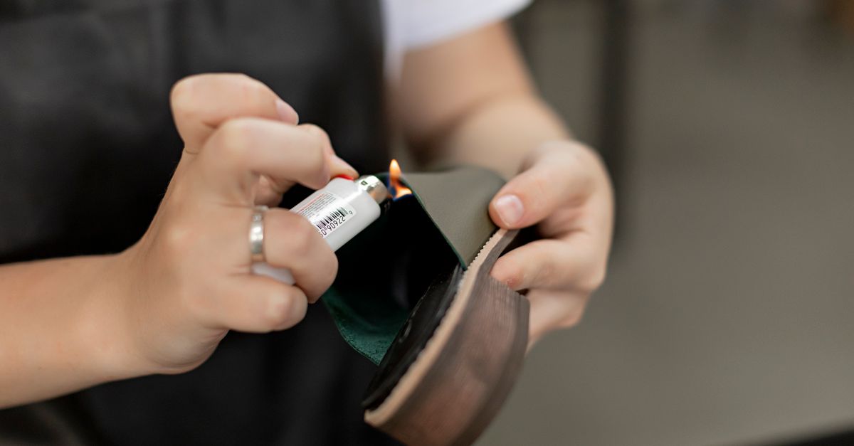 Detail of hands using a lighter for handmade shoe repair in a workshop.