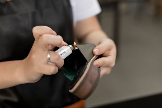 Detail of hands using a lighter for handmade shoe repair in a workshop.