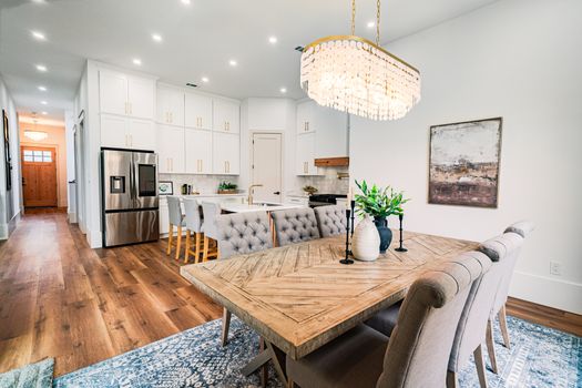 Spacious modern dining area with wooden table, plush chairs, and chandelier in a bright kitchen setting.