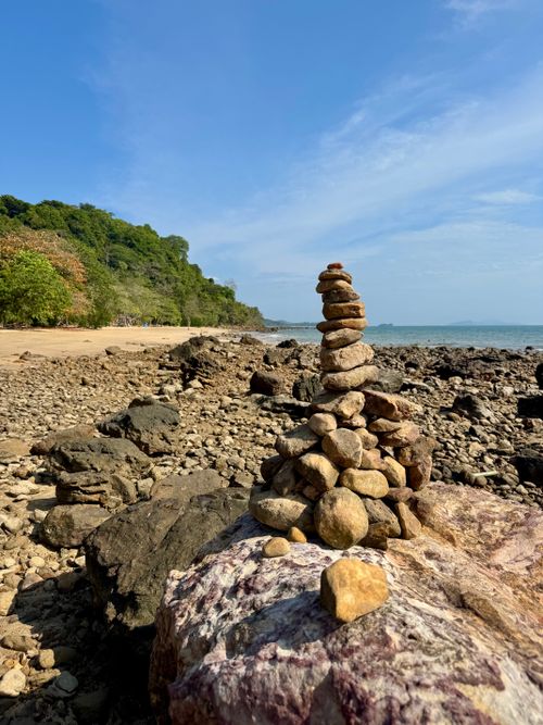 Free A serene stack of stones on a rocky seaside beach under a clear blue sky. Stock Photo
