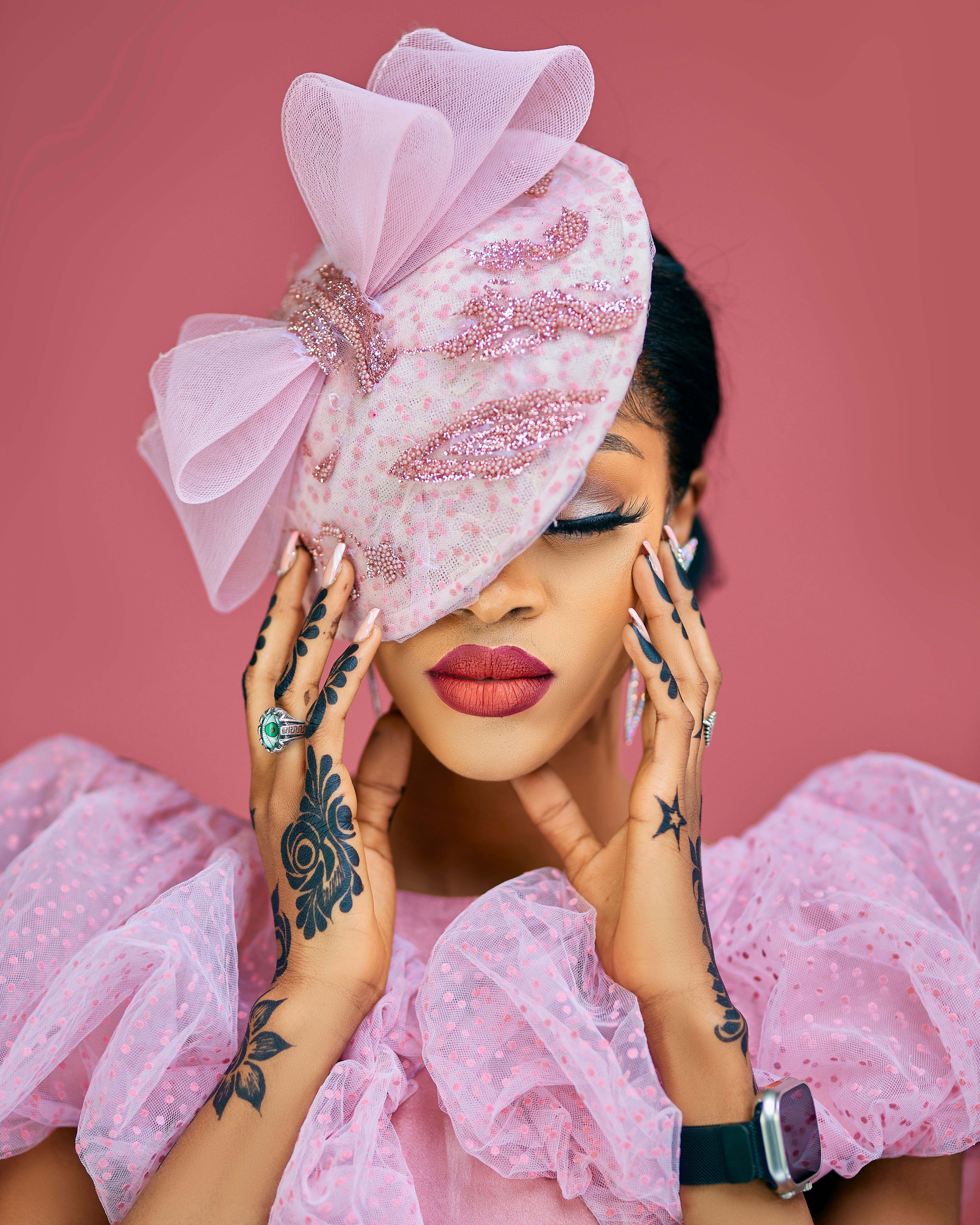 Stylish portrait of a woman in pink attire, featuring detailed tattoos and a decorative hat.