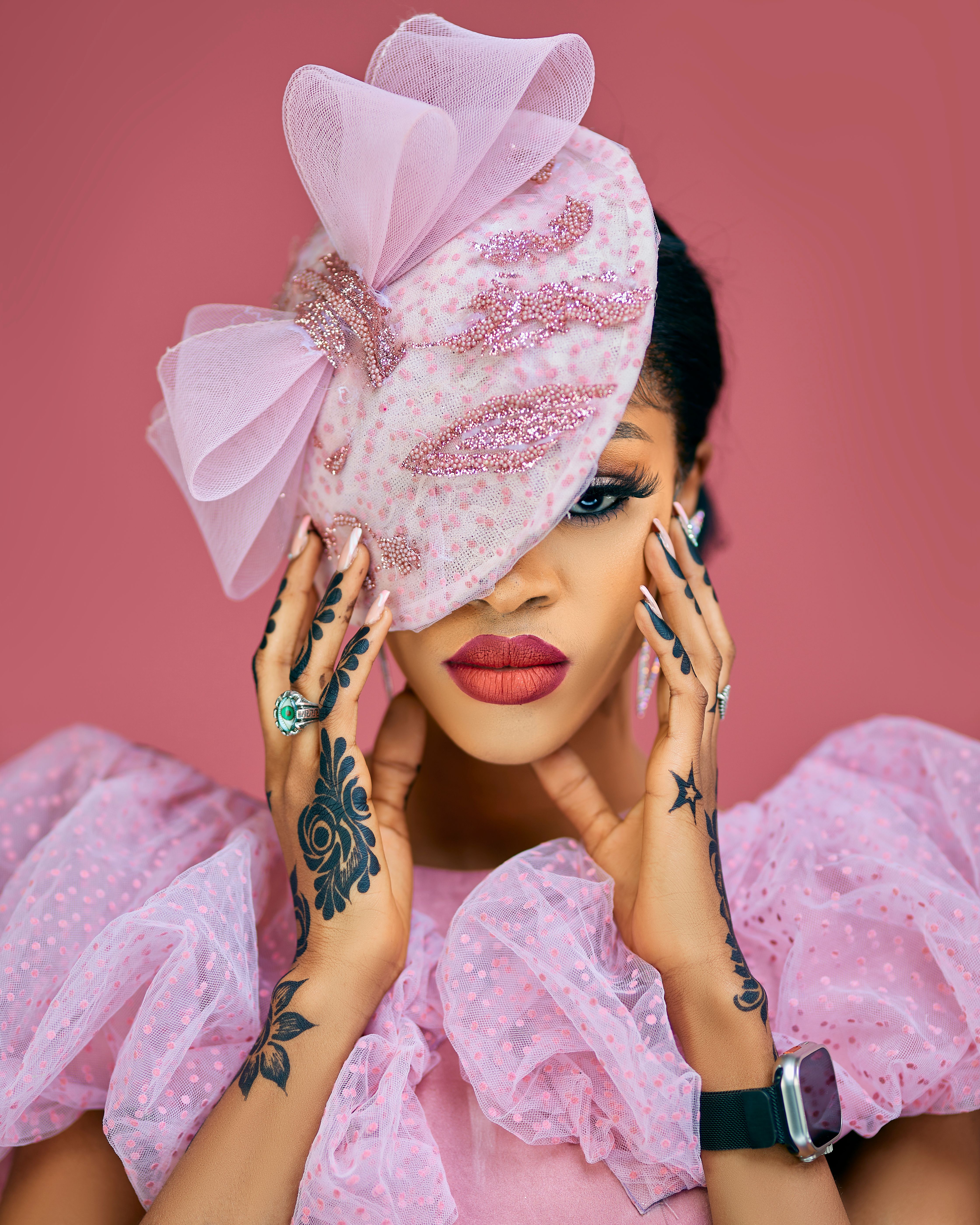 A fashionable woman in pink attire and hat, showcasing elegant tattoos and accessories.