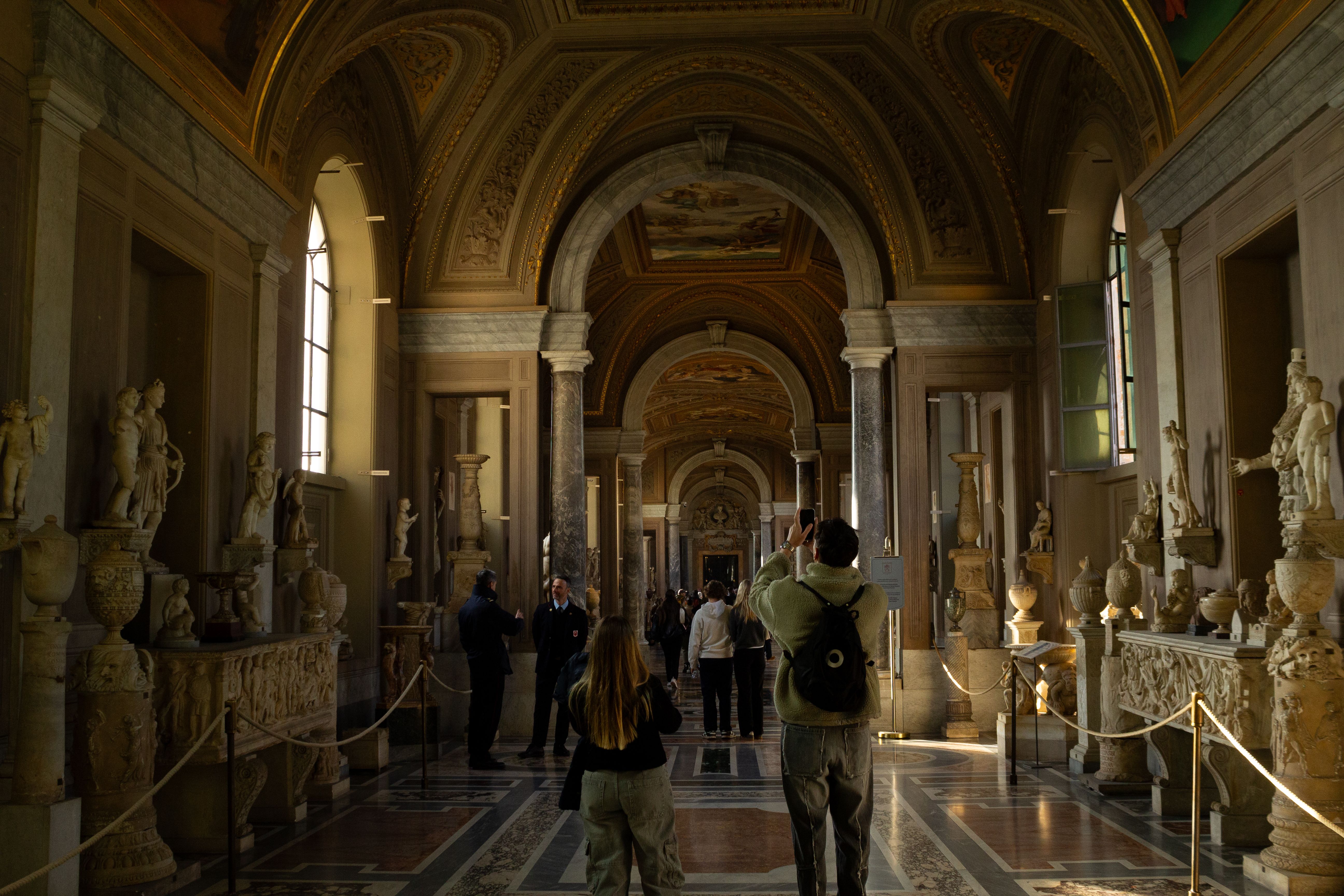 Visitors admire the ancient sculptures in a majestic hallway at the Vatican Museums.