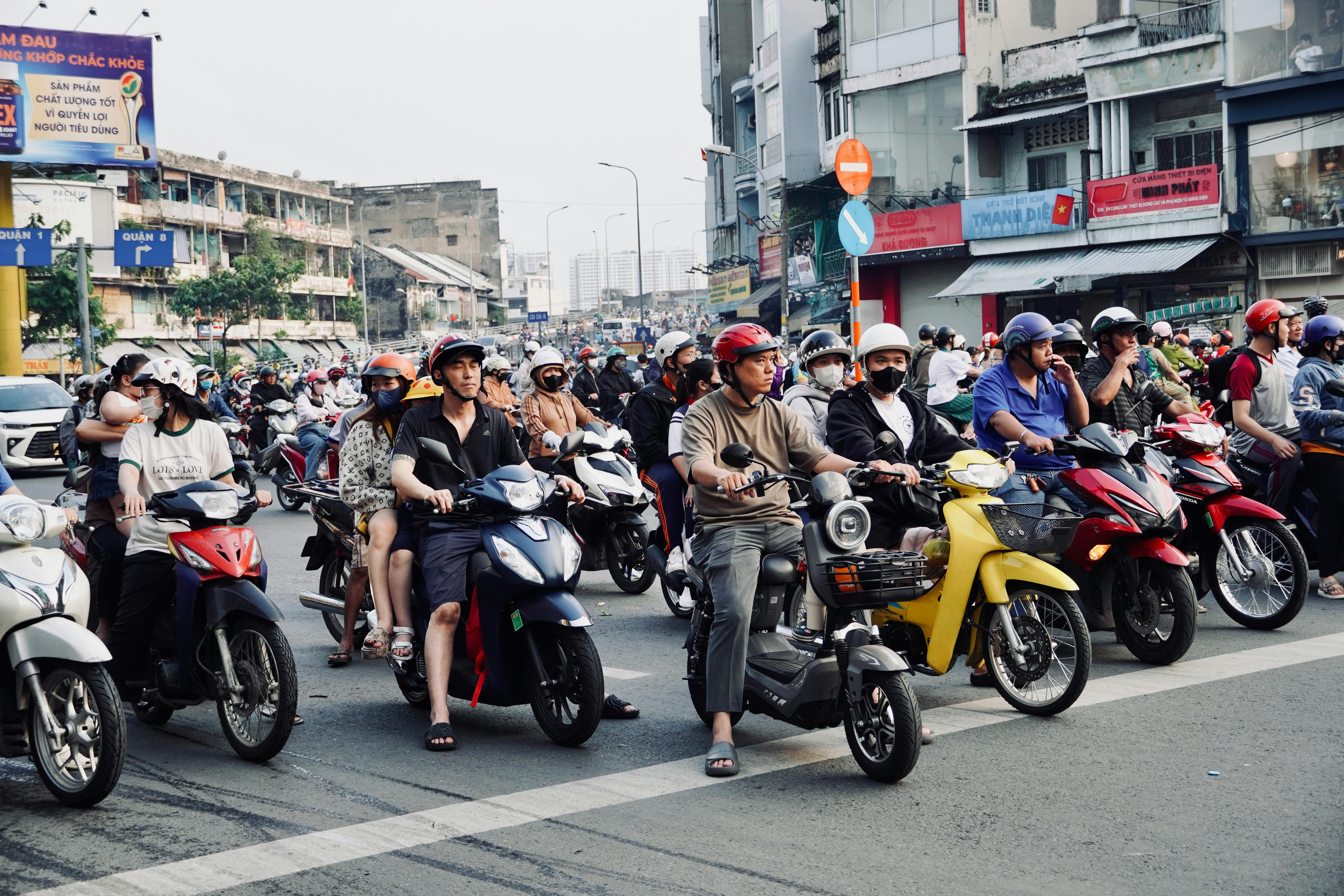 Scena di strada trafficata in un'area urbana con numerose moto e conducenti a un incrocio.