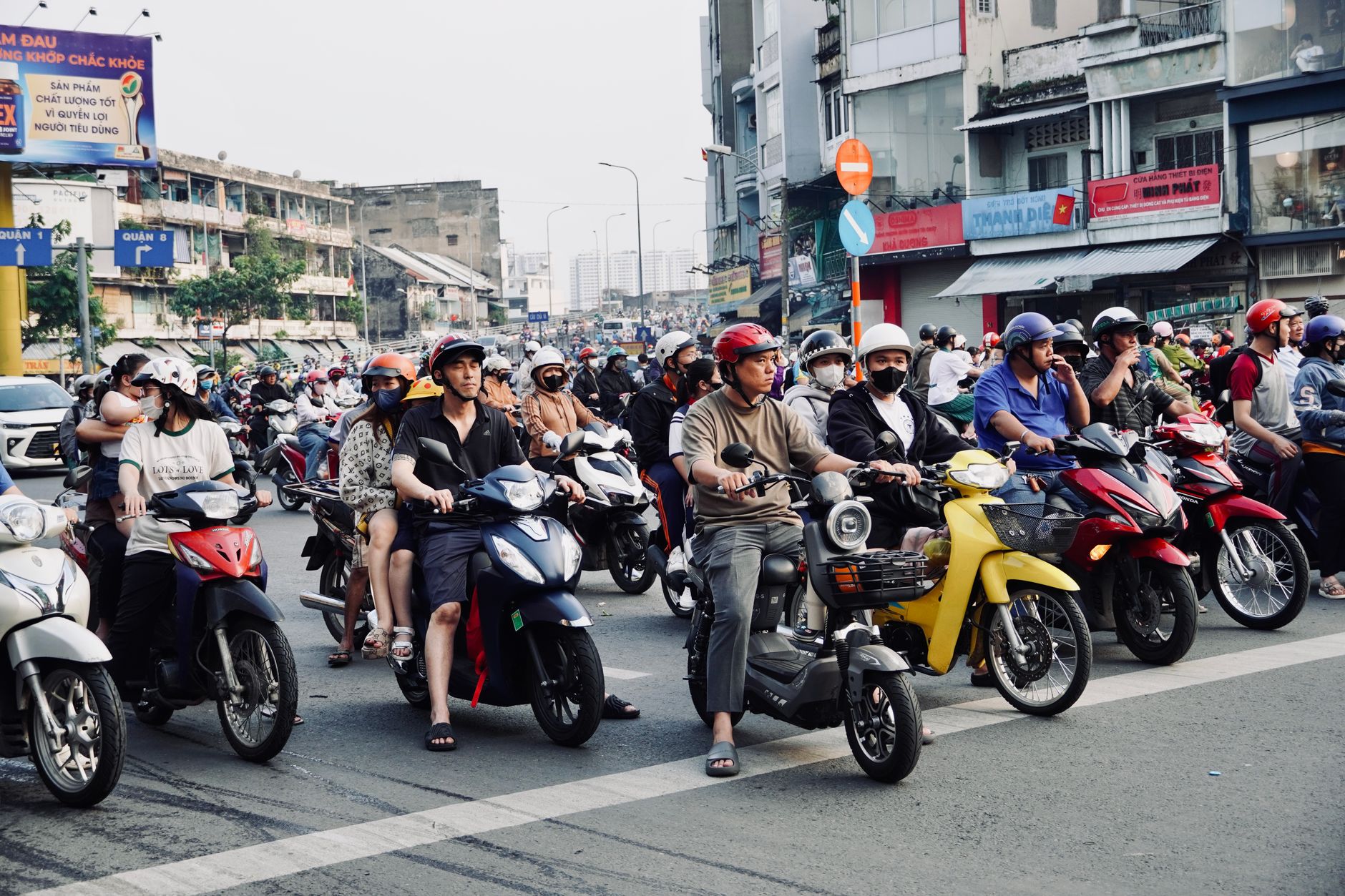 Busy street scene in an urban area with numerous motorbikes and riders at a traffic intersection.