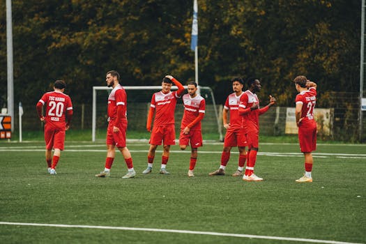 Amateur soccer team in red uniforms gathering on a green field during daytime.